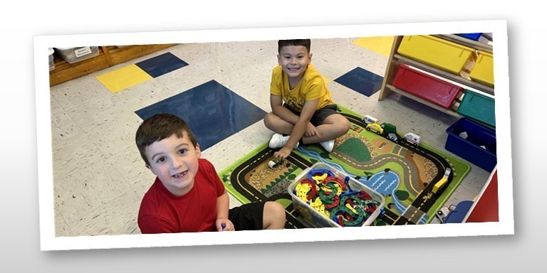 two kindergarten students playing on rug with cars