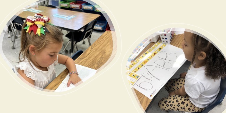 two kindergarten students sitting at table writing alphabet 