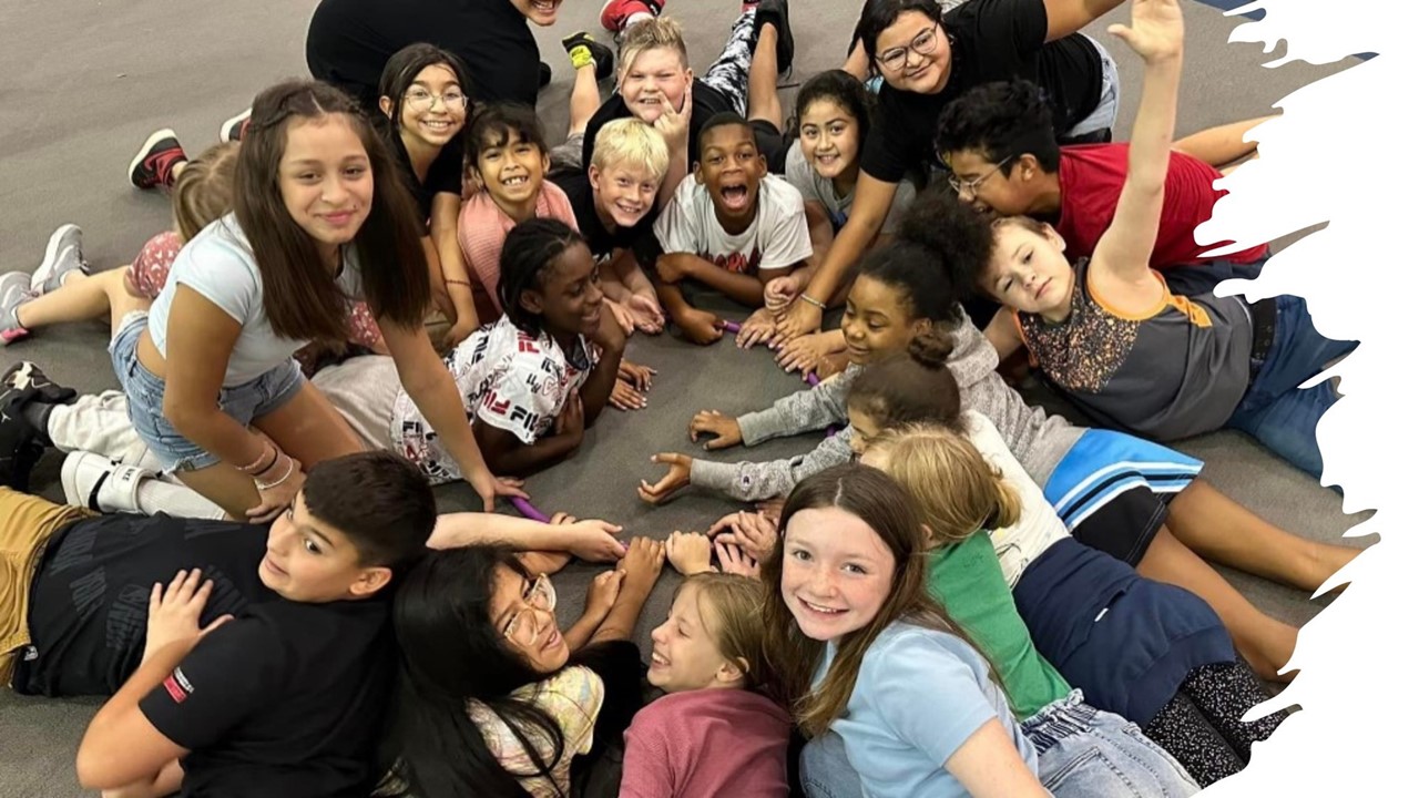 a fifth grade class of students on the floor in the multipurpose room laying in a circle looking happy as a pose for the picture