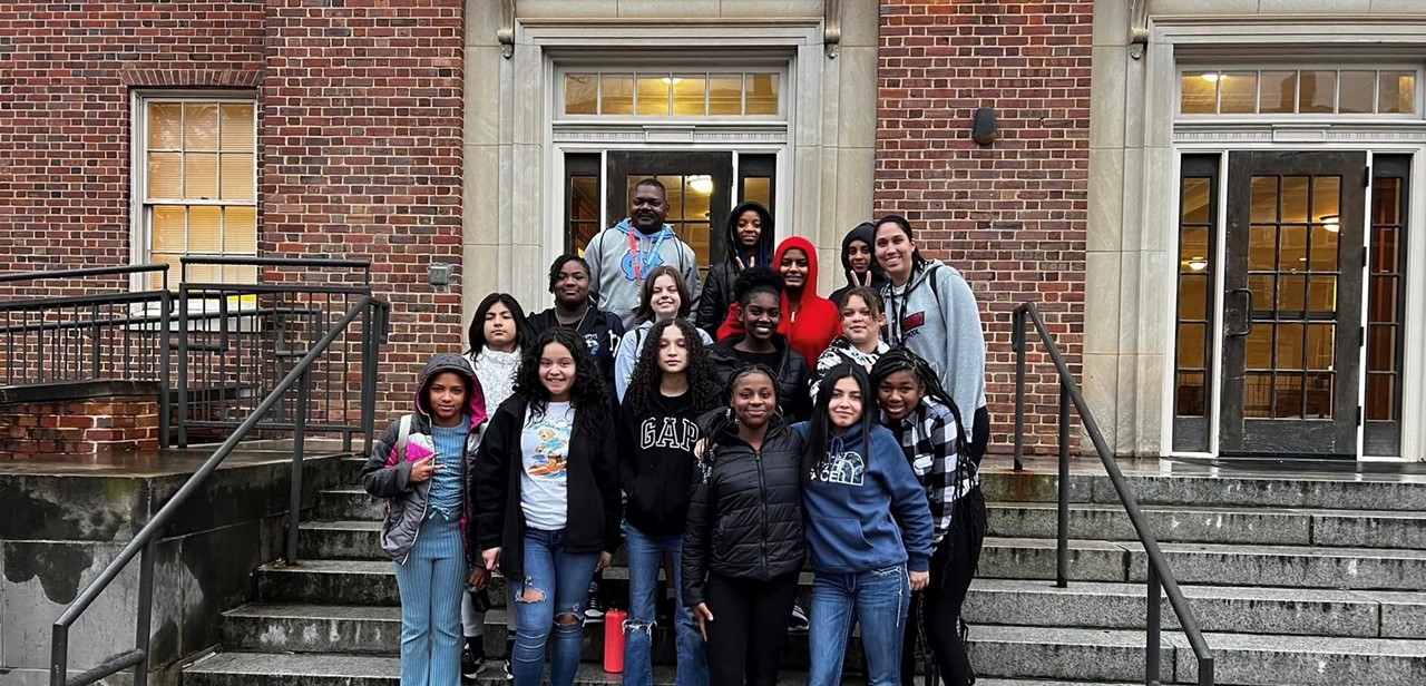 The Girls Basketball team stand in 4 rows on some stairs in front of a brink and concrete building at UNC Chapel Hil